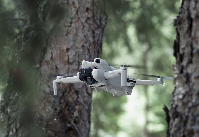 Valkoinen DJI Mini 4 Pro drone lentämässä kahden puun välistä