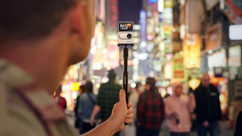 Insta360 GO 3 toimintakameran näyttö käännetty kohti kuvaajaa. Taustalla ihmisjoukko kaupungissa