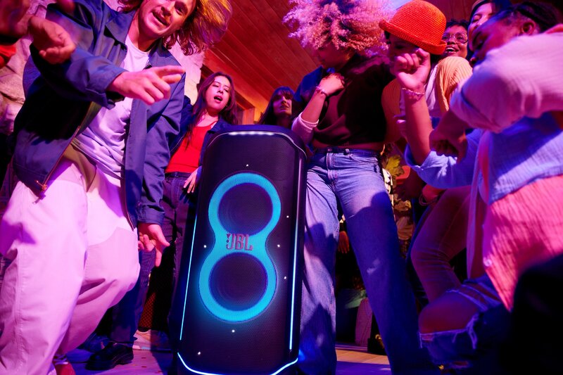 suurikokoinen, sinisillä valoilla varustettu JBL PartyBox Ultimate-kaiutin useiden juhlijoiden keskellä