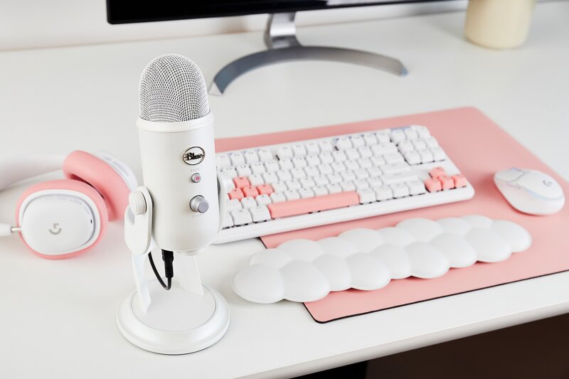 Valkoinen mikrofoni yhdessä valkoisen näppäimistön ja hiiren kanssa jotka ovat vaaleanpunaisen hiirimaton päällä