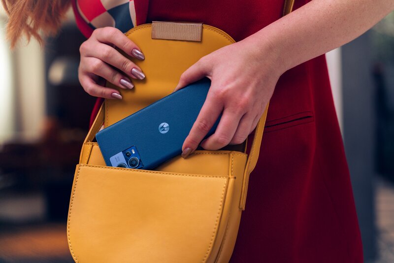 nainen laittamassa sinistä edge 30 fusion puhelinta keltaiseen laukkuun