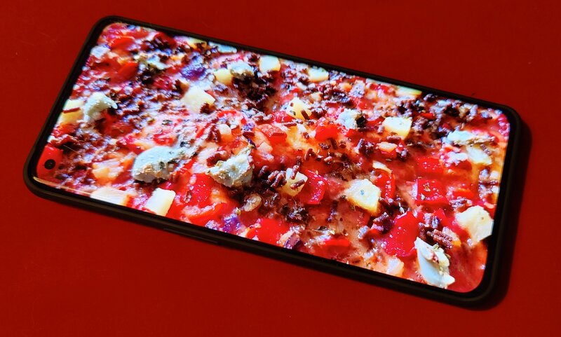 OnePlus 11 pöydällä, näyttö päällä, näytössä lähikuva pizzasta